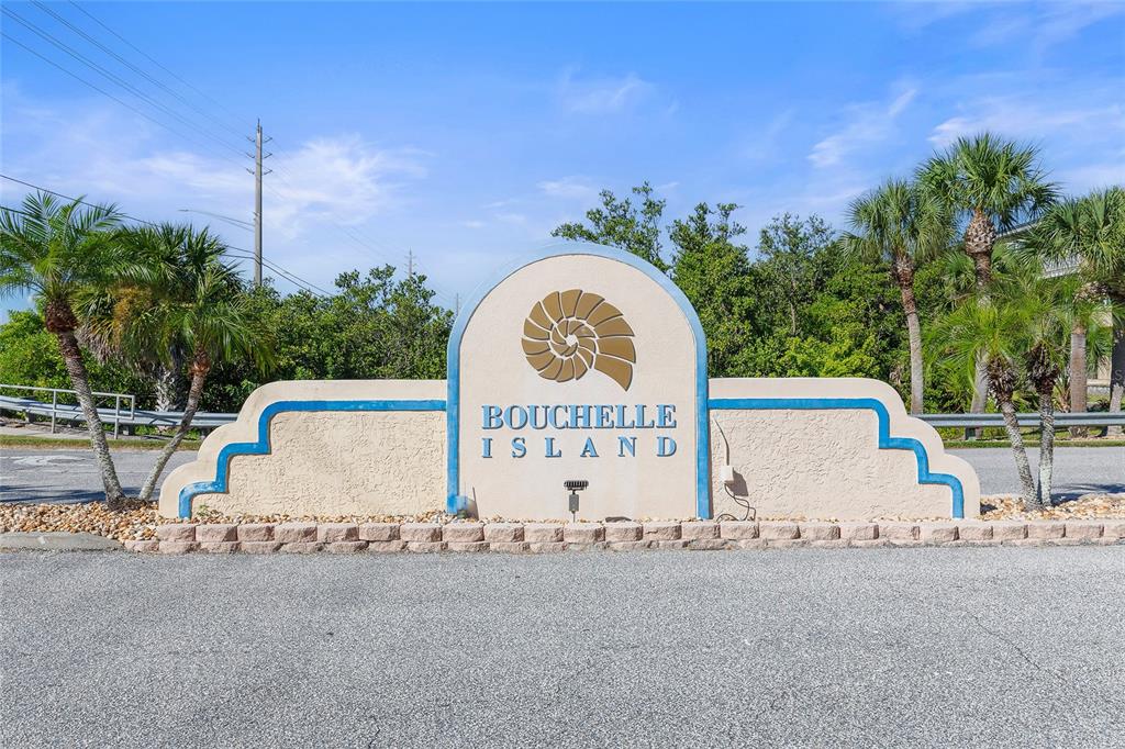 A beige monument sign with a nautilus shell logo marks the entrance to Bouchelle Island — 426 BOUCHELLE DRIVE UNIT 301, NEW SMYRNA BEACH, FL