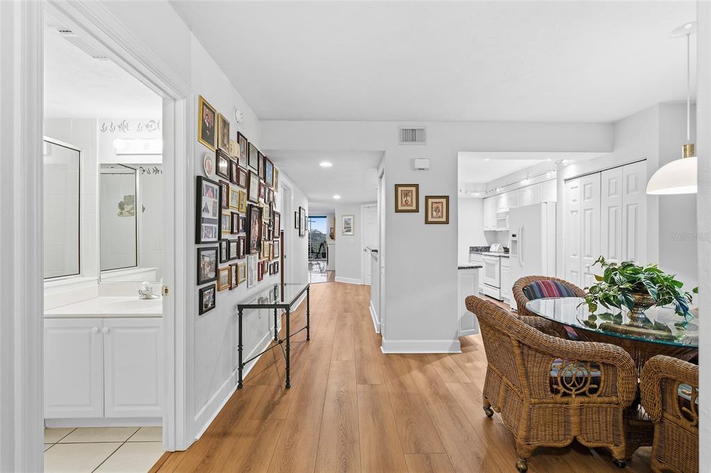 A hallway with a gallery wall leads to a dining area with wicker chairs — 426 BOUCHELLE DRIVE UNIT 301, NEW SMYRNA BEACH, FL