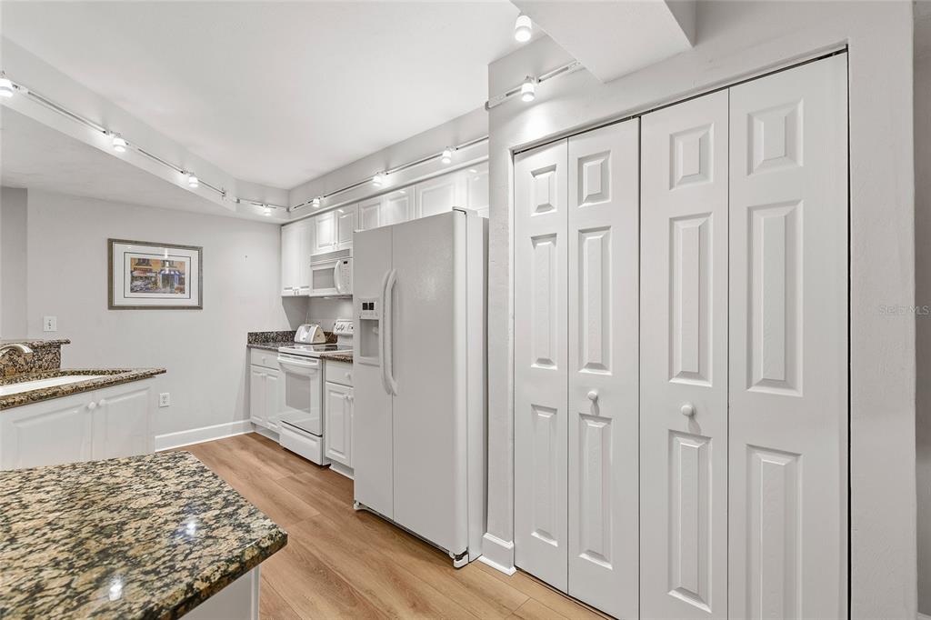 A kitchen with white cabinets, white appliances, granite countertops, and light wood-look flooring — 426 BOUCHELLE DRIVE UNIT 301, NEW SMYRNA BEACH, FL