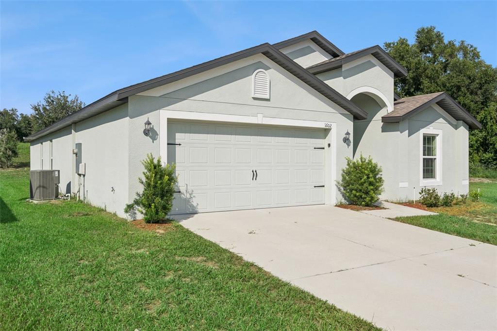 A single-story house with a light-colored stucco exterior, a two-car garage, and a concrete driveway — 1602 ORNE STREET, MASCOTTE, FL