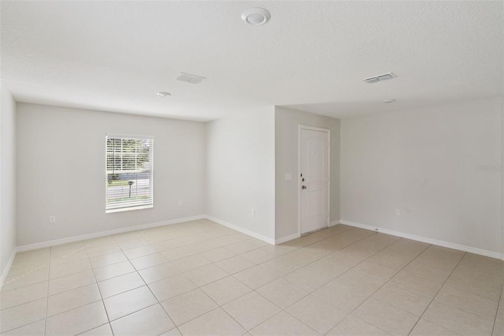 An empty room with light-colored tile flooring, white walls, a window, and a white door — 1602 ORNE STREET, MASCOTTE, FL