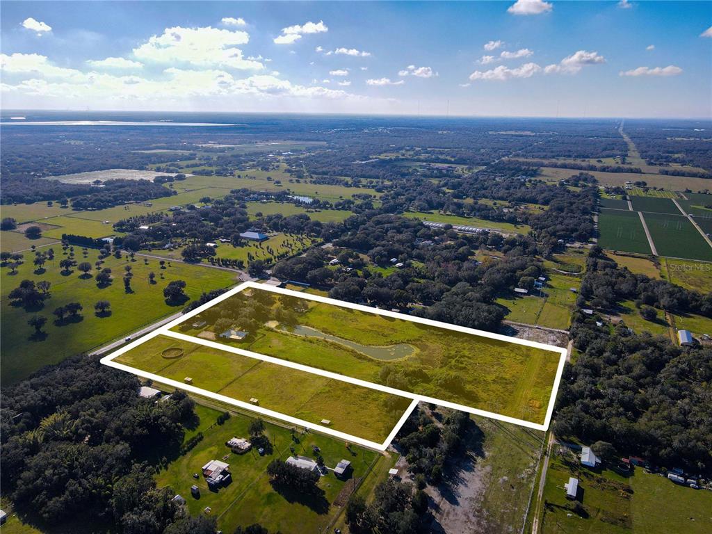 An aerial view shows a large, rectangular plot of land featuring a pond and pasture — 8719 & 8809 LITHIA PINECREST ROAD, LITHIA, FL