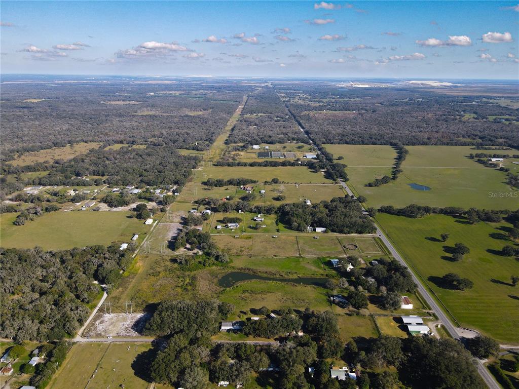 An aerial view shows a rural landscape with scattered houses, pastures, and a power line corridor — 8719 & 8809 LITHIA PINECREST ROAD, LITHIA, FL