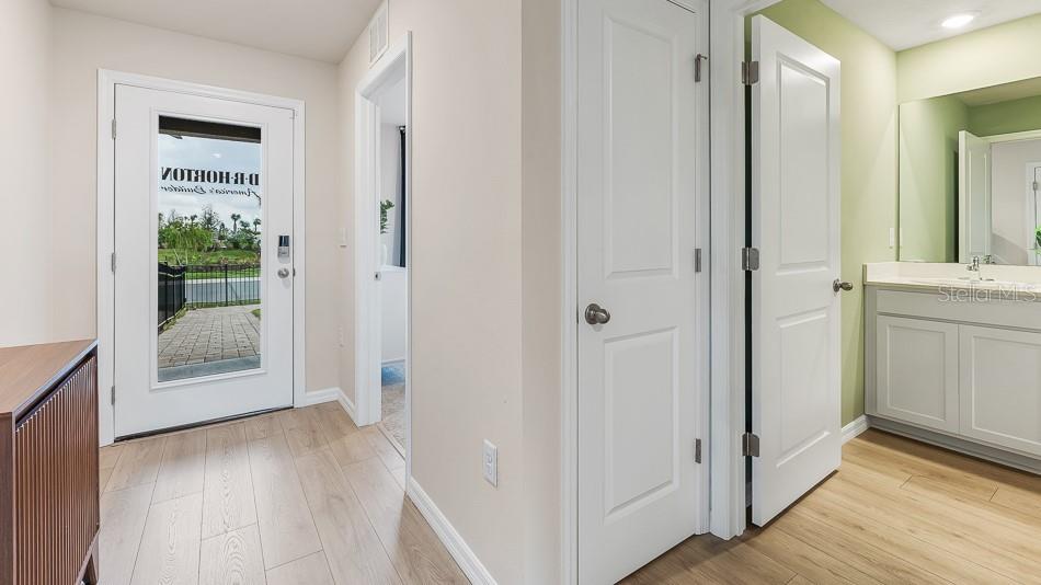An entryway features light wood flooring, a white front door, and an adjacent bathroom vanity — 10424 CURVING CREEK LOOP, PARRISH, FL