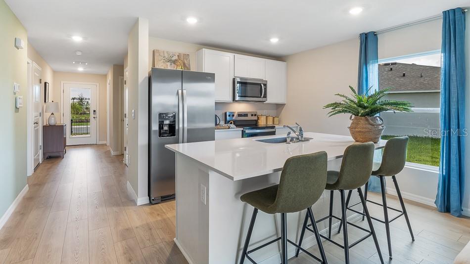 A kitchen with white cabinets, stainless steel appliances, and a central island with three stools — 10424 CURVING CREEK LOOP, PARRISH, FL