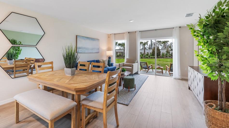 This open-concept living and dining area features light wood flooring, modern furniture, and sliding doors — 10424 CURVING CREEK LOOP, PARRISH, FL