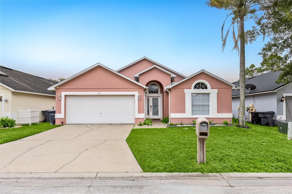 A single-story pink house with a two-car garage, a front lawn, and a concrete driveway — 611 SADDLE RIDGE DRIVE, DAVENPORT, FL