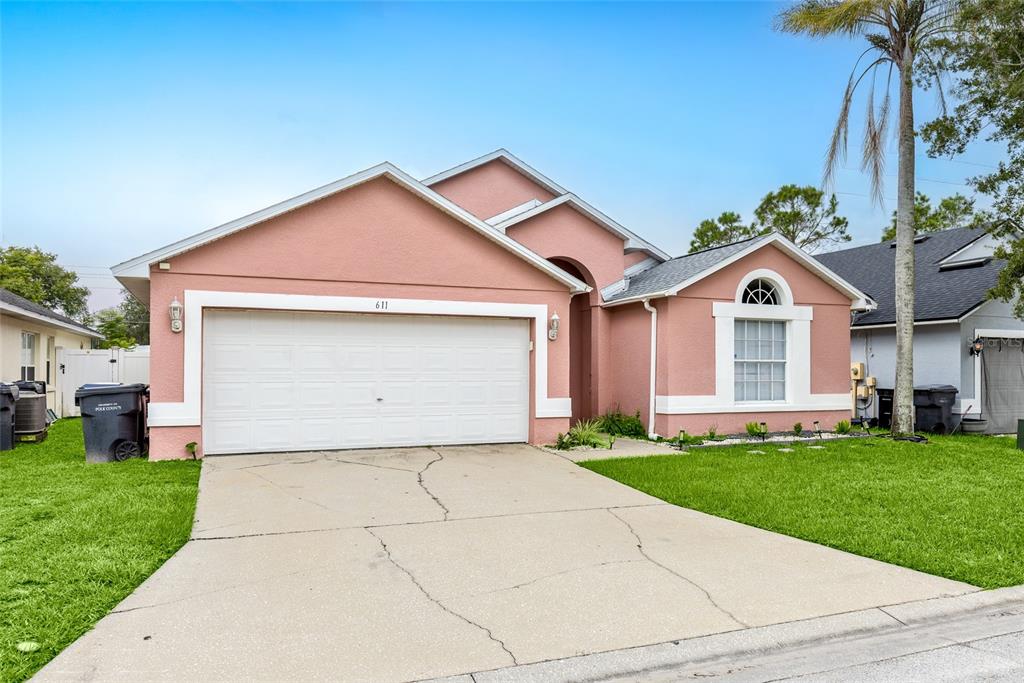 A pink, single-story house with a two-car garage and a concrete driveway — 611 SADDLE RIDGE DRIVE, DAVENPORT, FL