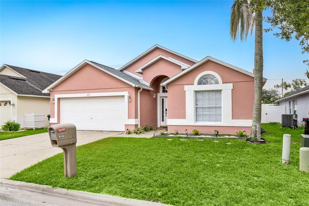 A pink single-story house with a two-car garage and a front lawn — 611 SADDLE RIDGE DRIVE, DAVENPORT, FL
