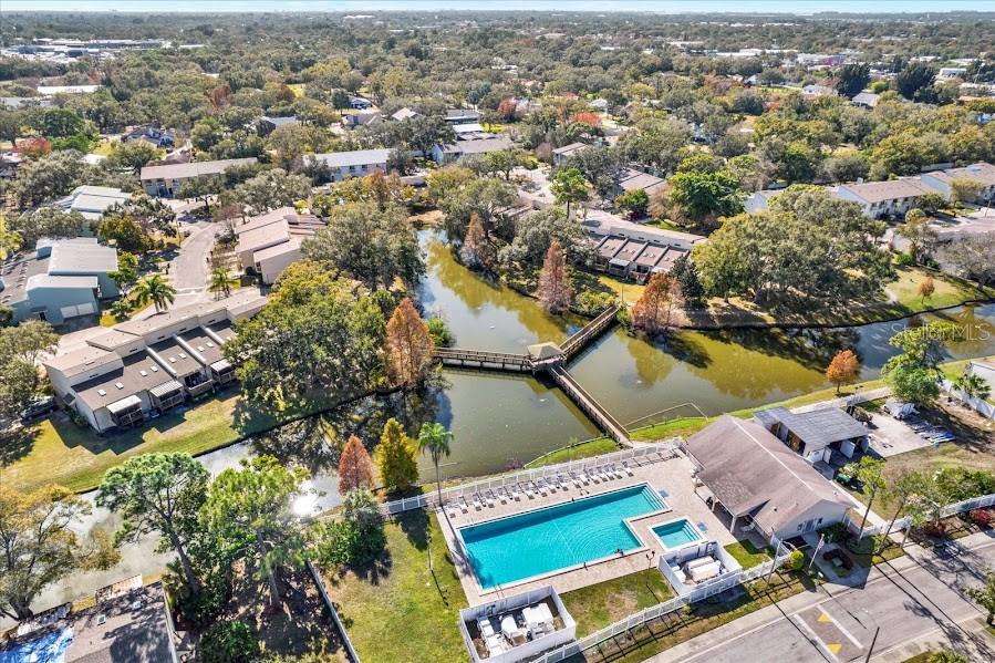 An aerial view shows a swimming pool, a clubhouse, and a wooden bridge over a pond — 6311 93RD TERRACE N UNIT 4403, PINELLAS PARK, FL