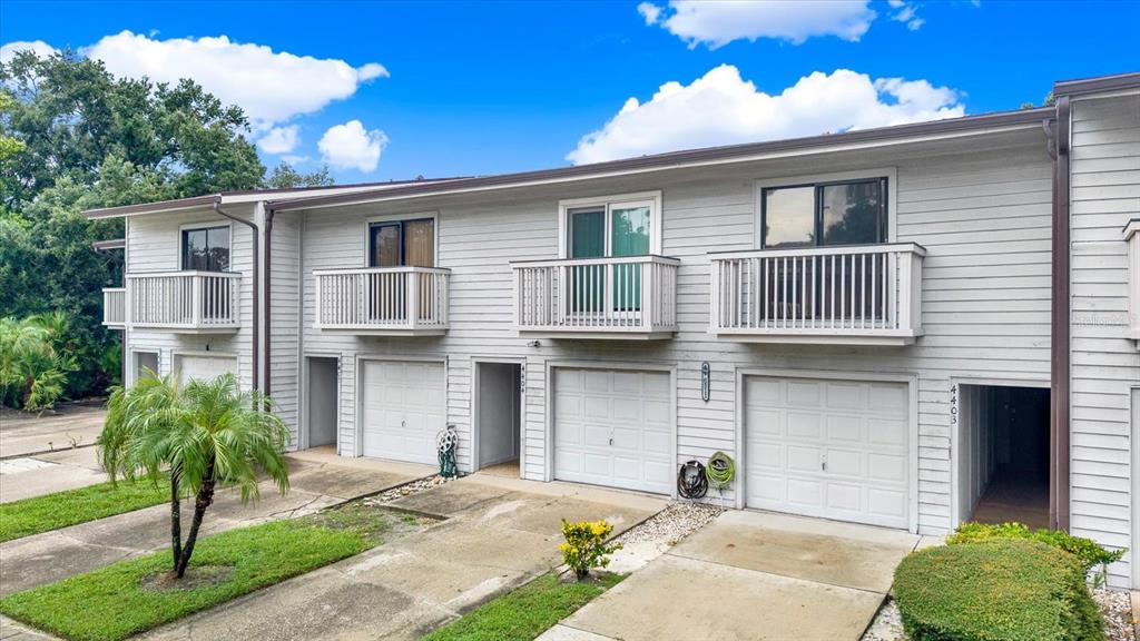 A row of two-story townhouses with light gray siding, balconies, and attached ground-level garages — 6311 93RD TERRACE N UNIT 4403, PINELLAS PARK, FL