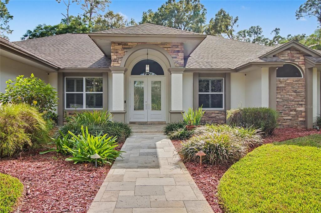 A stone-accented house exterior features a central arched entryway with double doors and a walkway — 5186 TALLOWOOD WAY, NAPLES, FL