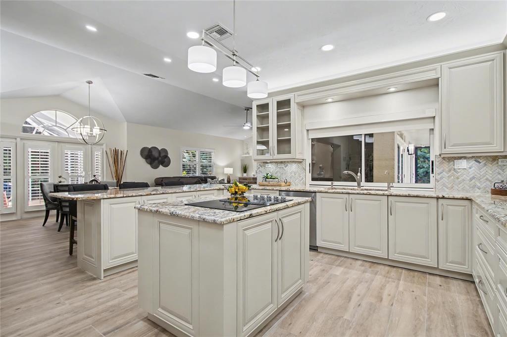 A kitchen features light-colored cabinetry, granite countertops, a central island, and wood-look tile flooring — 5186 TALLOWOOD WAY, NAPLES, FL