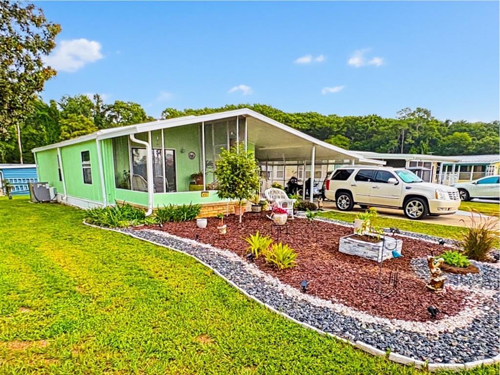 A light green mobile home features a screened-in porch and a landscaped front yard — 413 S TIMBER TRAIL, WILDWOOD, FL