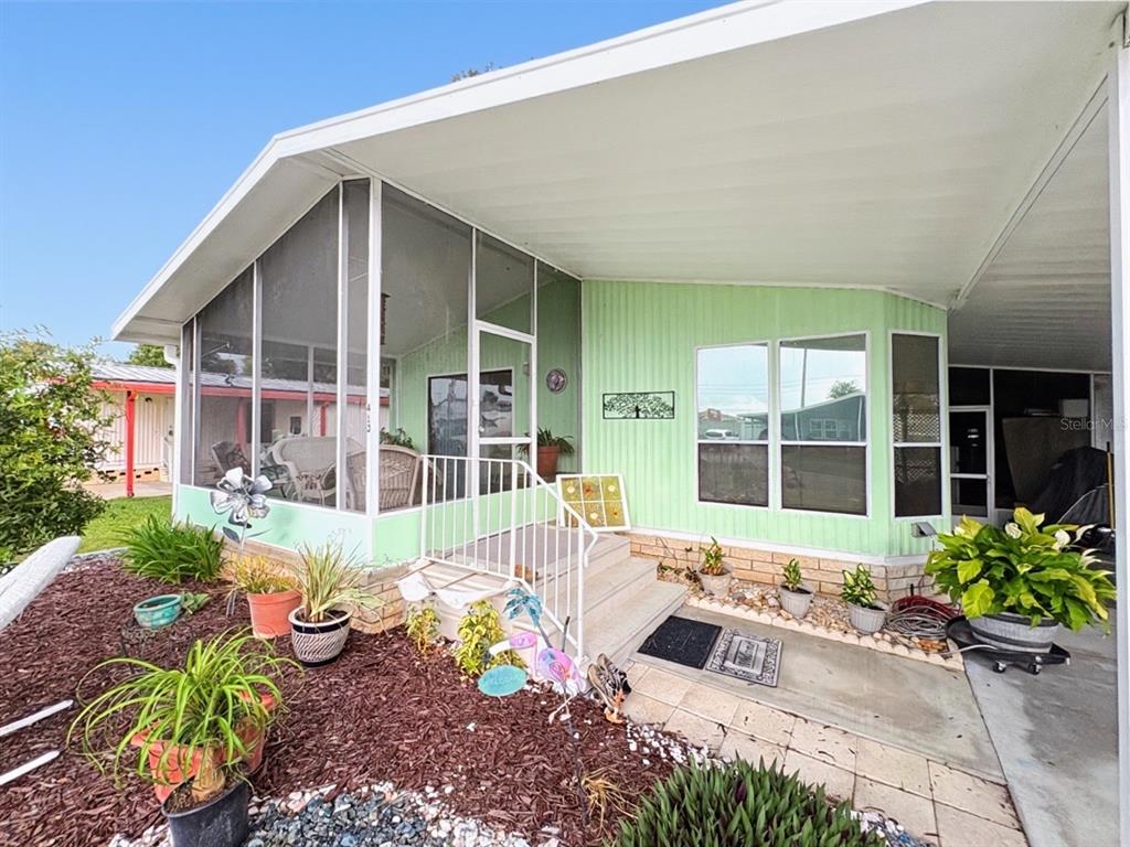 A light green mobile home exterior features a screened-in porch, white railings, and potted plants — 413 S TIMBER TRAIL, WILDWOOD, FL