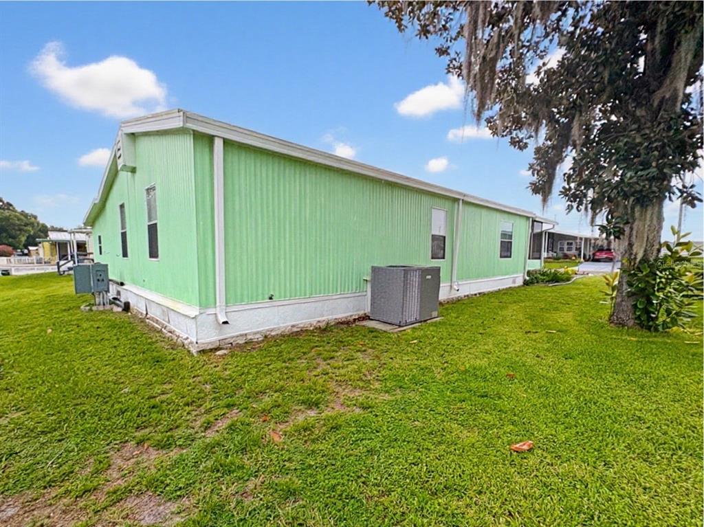 The exterior of a light green mobile home features a central air conditioning unit — 413 S TIMBER TRAIL, WILDWOOD, FL