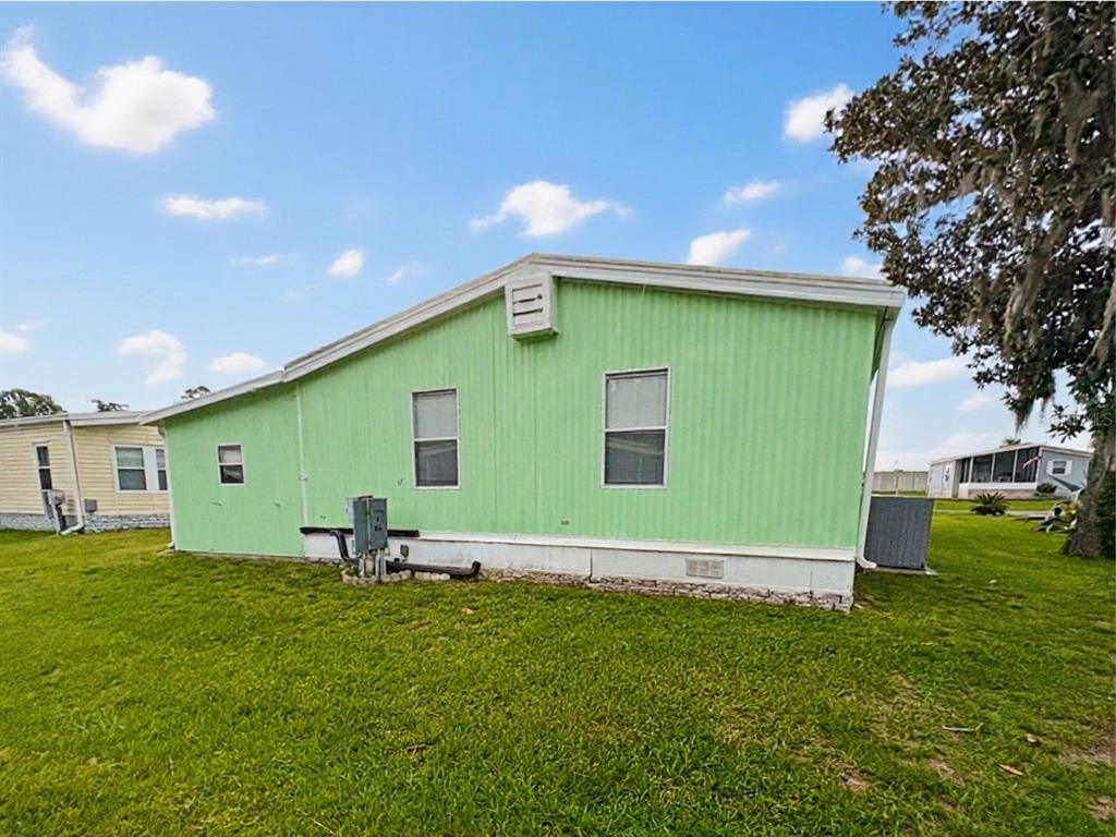 The exterior of a light green manufactured home features a gable roof and two windows — 413 S TIMBER TRAIL, WILDWOOD, FL