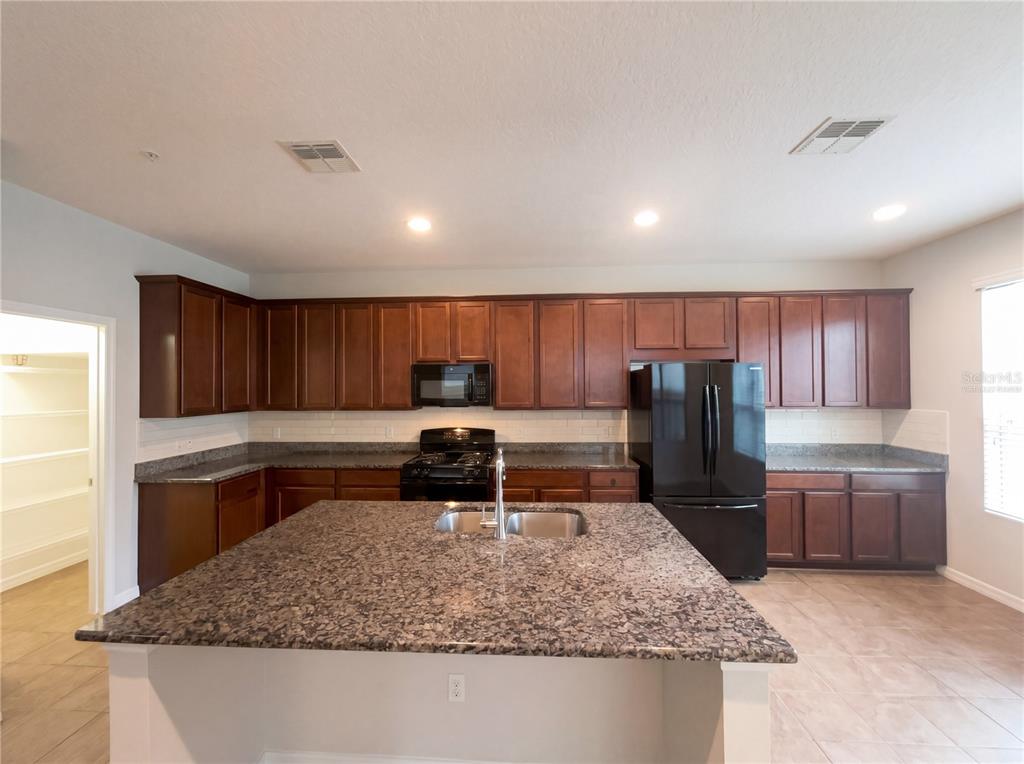 A kitchen features dark wood cabinets, granite countertops, a center island, and black appliances — 5545 BOWMAN DRIVE, WINTER GARDEN, FL
