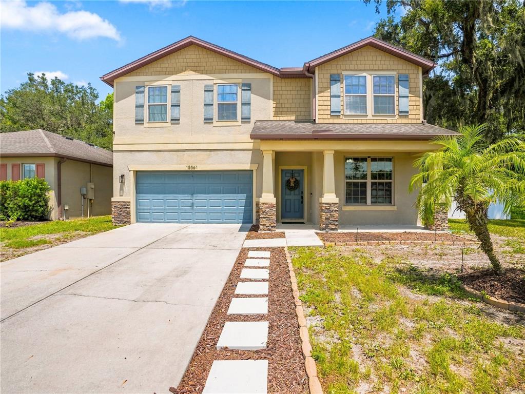 A two-story suburban house features a blue garage door, tan stucco siding, and a walkway — 15561 STONE HOUSE DRIVE, BROOKSVILLE, FL