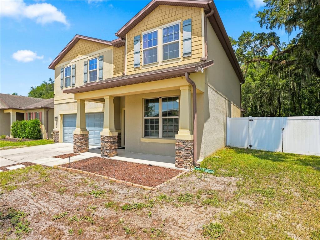 A two-story house with a tan stucco exterior, stone-accented porch columns, and a white fence — 15561 STONE HOUSE DRIVE, BROOKSVILLE, FL