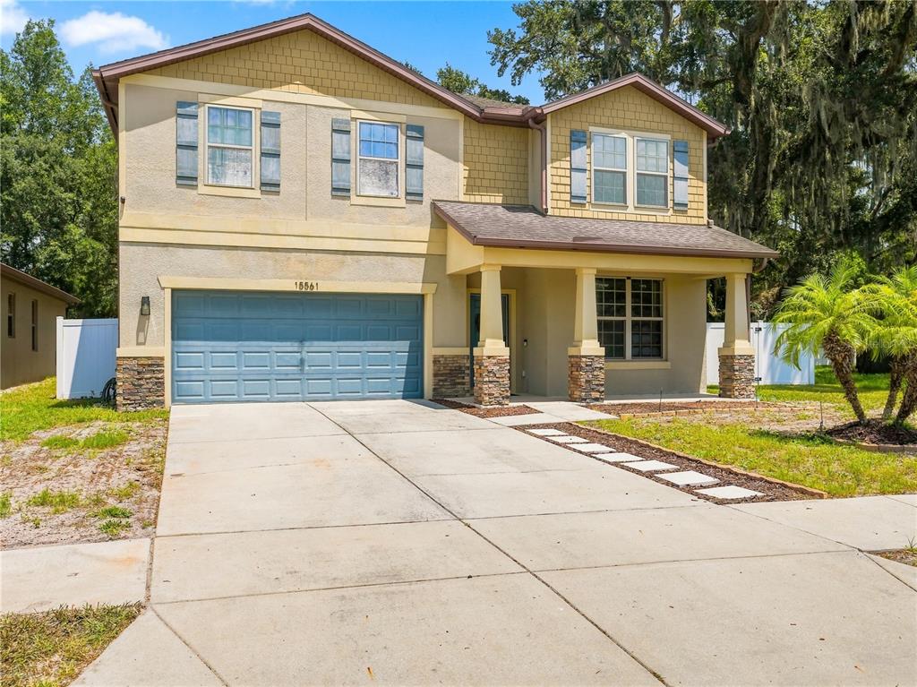 A two-story house with a blue garage door, stone accents, and a concrete driveway — 15561 STONE HOUSE DRIVE, BROOKSVILLE, FL