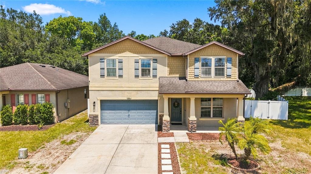 A two-story suburban house with a gray garage, tan siding, and a covered front porch — 15561 STONE HOUSE DRIVE, BROOKSVILLE, FL
