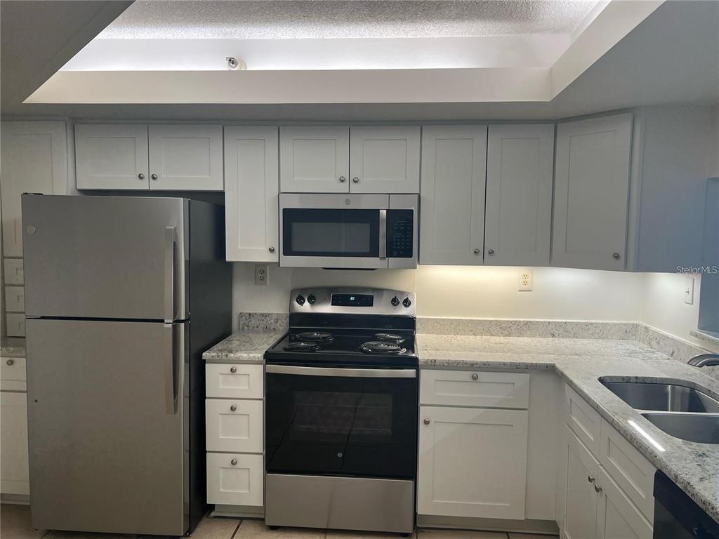 A kitchen features white cabinets, stainless steel appliances, and speckled granite countertops — 690 ISLAND WAY UNIT 208, CLEARWATER, FL