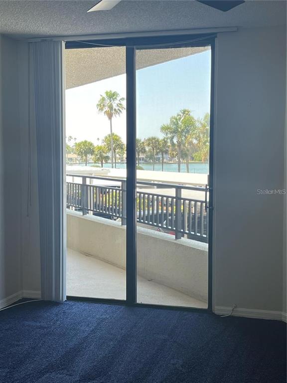A room with blue carpet features a sliding glass door opening to a waterfront balcony — 690 ISLAND WAY UNIT 208, CLEARWATER, FL