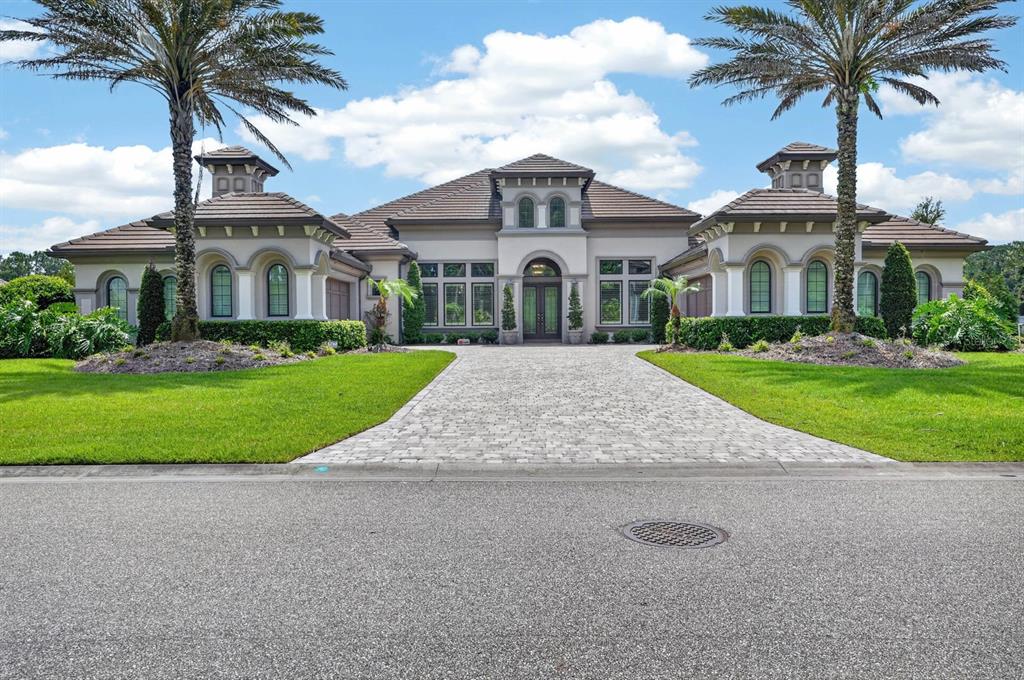 A large, single-story Mediterranean-style house with a paved driveway and two palm trees — 1023 SUDBURY LANE, ORMOND BEACH, FL