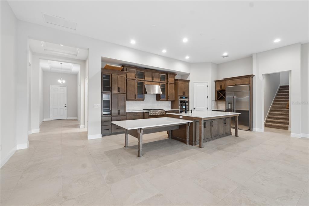 A kitchen features dark wood cabinetry, a large island with an attached table, and tile flooring — 1953 ARCHING BRANCH DRIVE, ZEPHYRHILLS, FL
