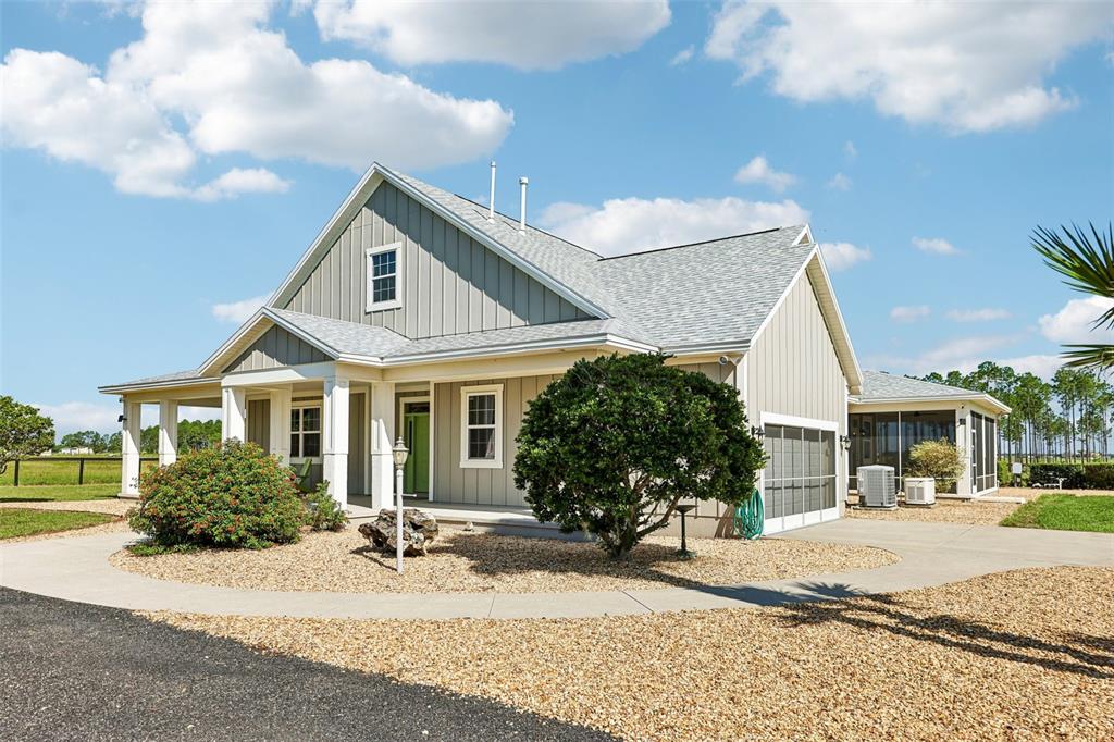 A light-colored house with vertical siding, a gravel yard, and a screened-in porch — 2088 NW 102ND BOULEVARD, WILDWOOD, FL