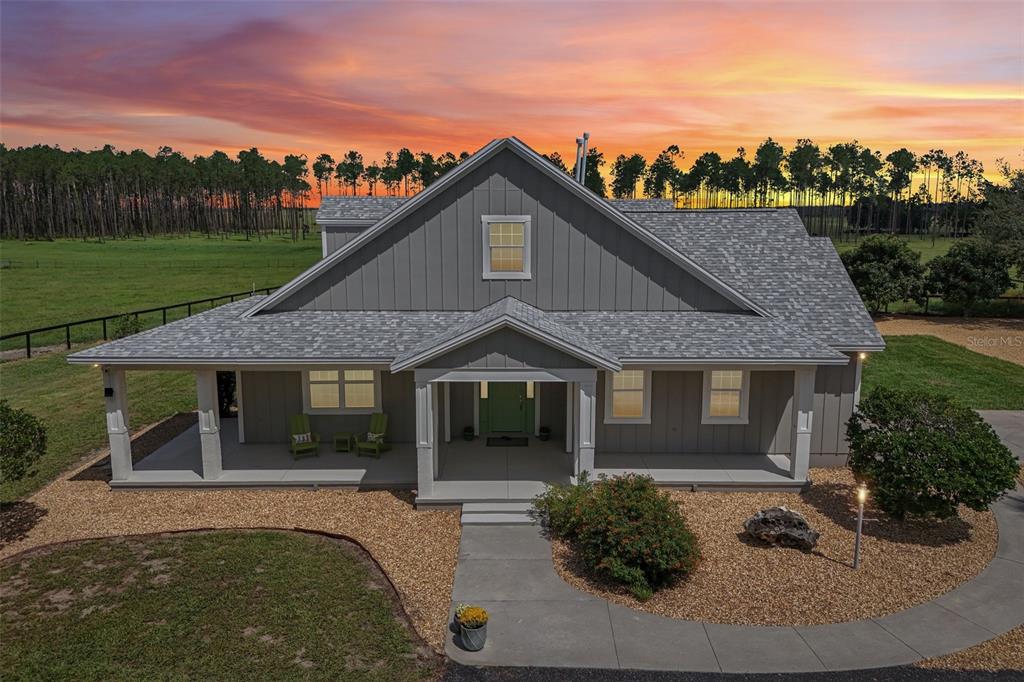 An exterior view of a gray farmhouse with a covered porch and a sunset sky — 2088 NW 102ND BOULEVARD, WILDWOOD, FL