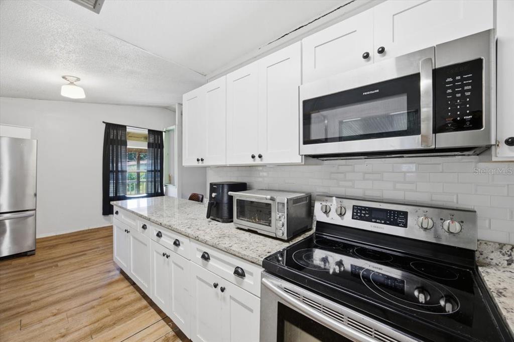 A kitchen features white cabinets, granite countertops, stainless steel appliances, and a subway tile backsplash — 6709 FIVE ACRE RD, PLANT CITY, FL
