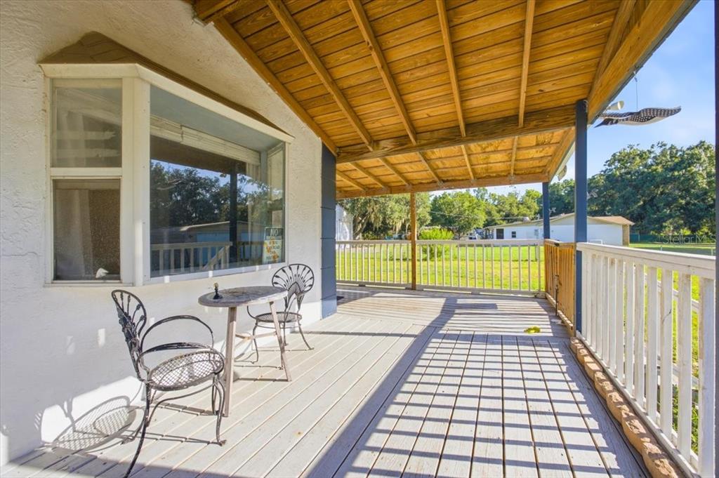 A covered wooden porch features a small bistro set and a large bay window — 6709 FIVE ACRE RD, PLANT CITY, FL
