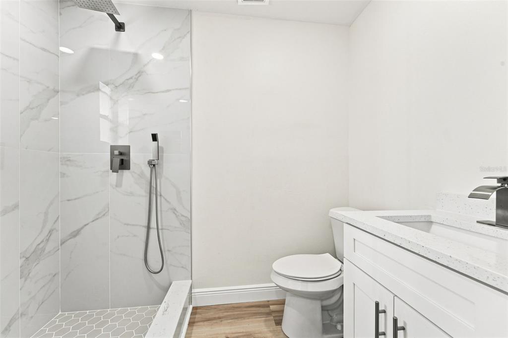 A bathroom features a walk-in shower with marble-look tile, a white vanity, and wood-look flooring — 2781 KING OAK CIRCLE, ST CLOUD, FL