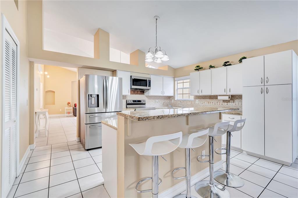 A kitchen with white cabinets, granite countertops, stainless steel appliances, and three bar stools — 3101 CAYMAN WAY, ORLANDO, FL