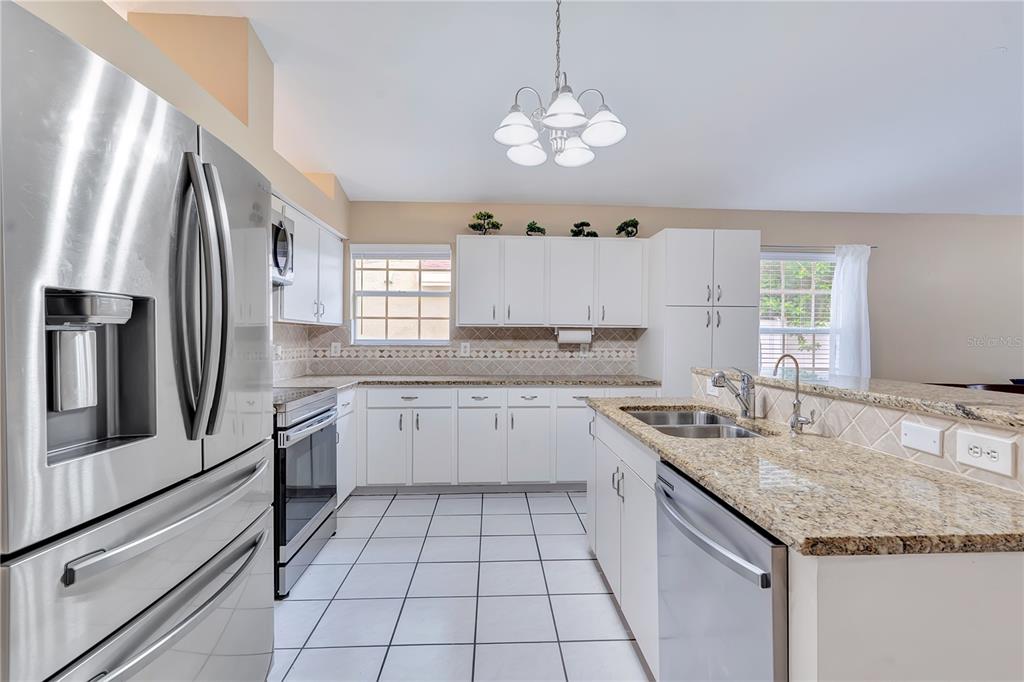 A kitchen featuring white cabinets, granite countertops, stainless steel appliances, and white tile flooring — 3101 CAYMAN WAY, ORLANDO, FL