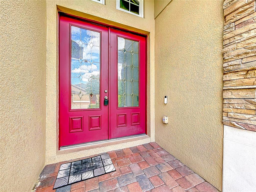 A red double front door with glass panels sits on a brick porch — 2432 EMERALD ROSE WAY, APOPKA, FL