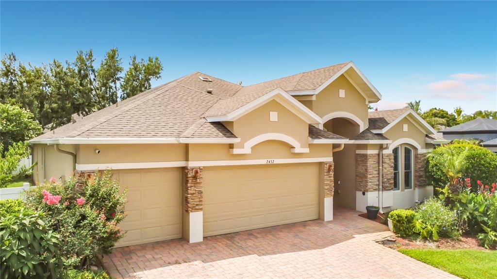 A tan single-story house with a two-car garage, stone accents, and a paved driveway — 2432 EMERALD ROSE WAY, APOPKA, FL