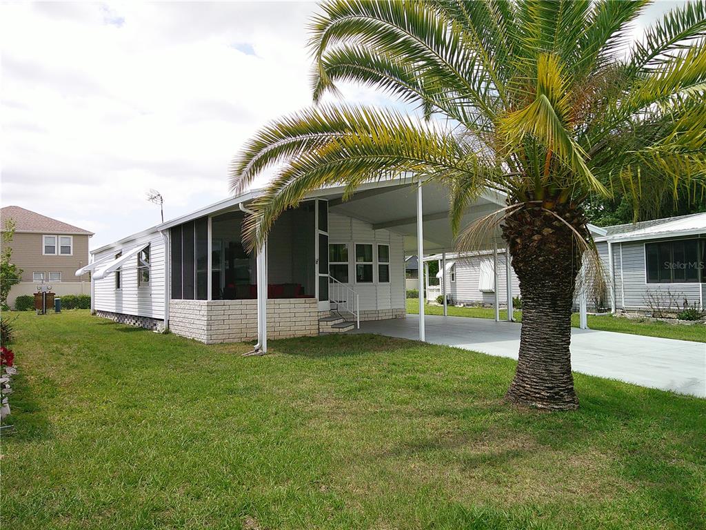 A white mobile home features a screened-in porch, a carport, and a large palm tree — 3205 HICKORY DRIVE, WESLEY CHAPEL, FL