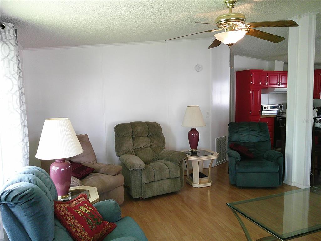 A living room features multiple armchairs, a ceiling fan, and a view into a red kitchen — 3205 HICKORY DRIVE, WESLEY CHAPEL, FL