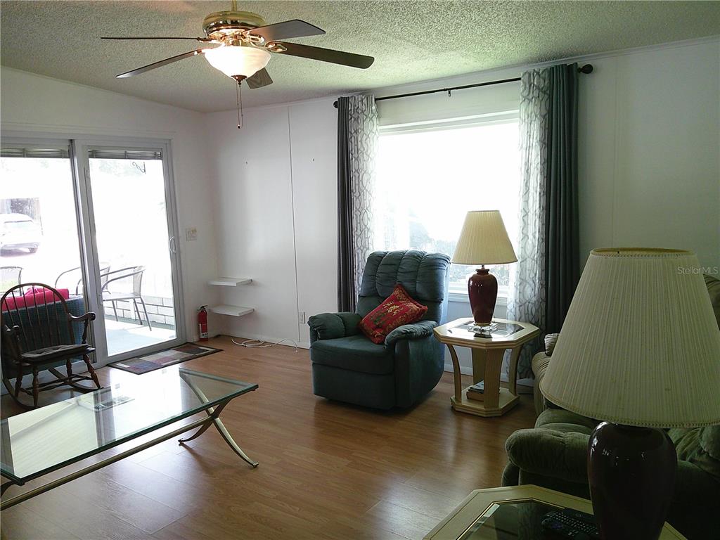 A living room features wood-look flooring, a ceiling fan, a recliner, and a glass-topped table — 3205 HICKORY DRIVE, WESLEY CHAPEL, FL