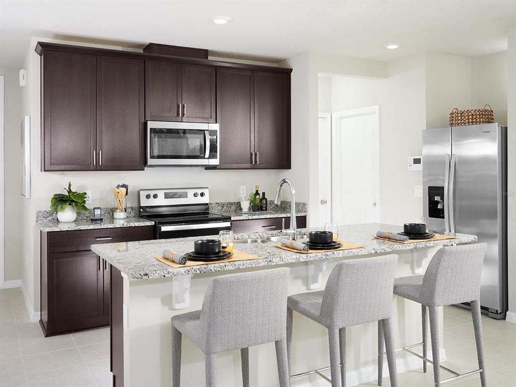A kitchen features dark wood cabinets, granite countertops, a stainless steel island, and three chairs — 4559 RANGELAND WAY, ST CLOUD, FL