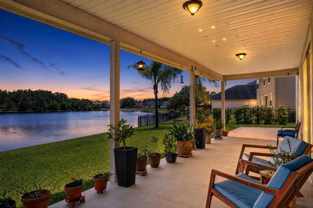A covered patio overlooks a lake at sunset with potted plants and wooden outdoor furniture — 3016 TOWER OAKS DRIVE, ORANGE PARK, FL