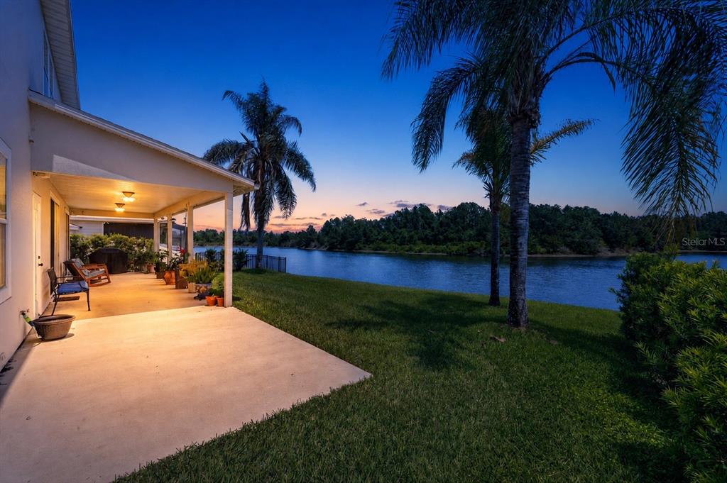A covered patio overlooks a grassy lawn, a lake, and palm trees at sunset — 3016 TOWER OAKS DRIVE, ORANGE PARK, FL