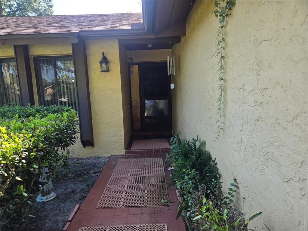 A yellow stucco house exterior features a tiled walkway leading to a dark front door — 827 RILL DRIVE, ALTAMONTE SPRINGS, FL