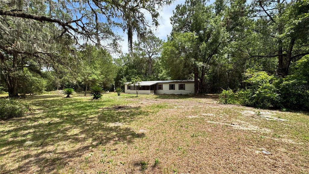 A single-story house with a screened porch sits on a large, wooded lot — 11286 E HIGHWAY 25, BELLEVIEW, FL