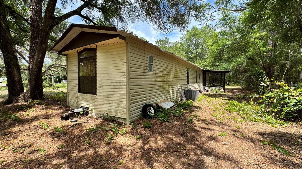 An exterior view of a weathered, light-colored mobile home situated in a wooded lot — 11286 E HIGHWAY 25, BELLEVIEW, FL