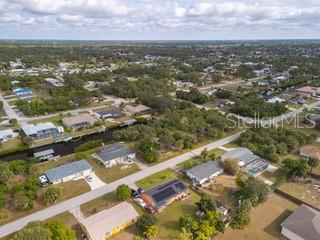 An aerial view shows a residential neighborhood with houses, a canal, and surrounding vegetation — 18262 VAN NUYS CIRCLE, PORT CHARLOTTE, FL