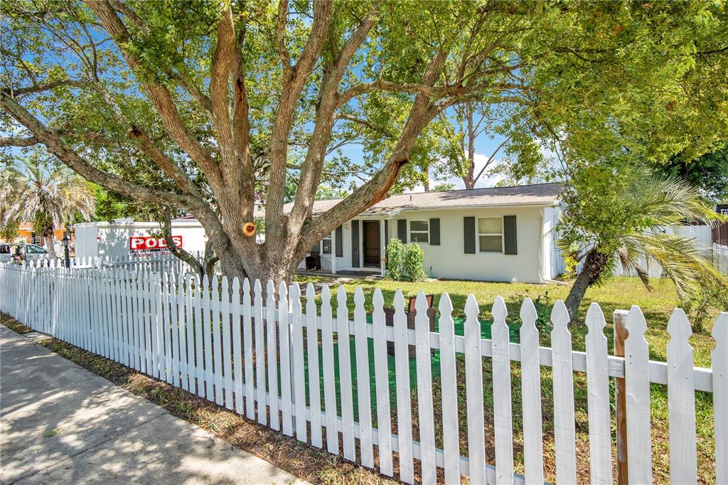 A single-story house with a white picket fence, a carport, and mature trees in front — 682 MERRIMAC STREET, DELTONA, FL